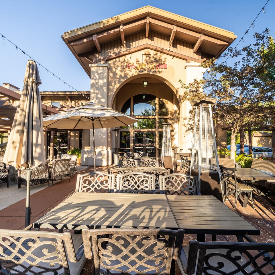 The Yellow Chilli Indian restaurant exterior with a spacious patio, ornate tables, umbrellas, heaters, and string lights.