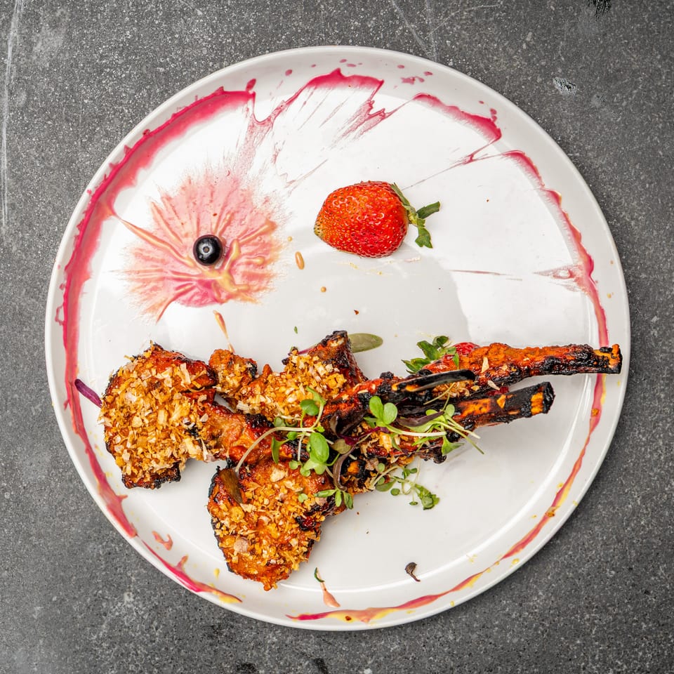 Grilled skewered meat and vegetables topped with crispy garnish and microgreens, served with berries and colorful sauce on a white plate.