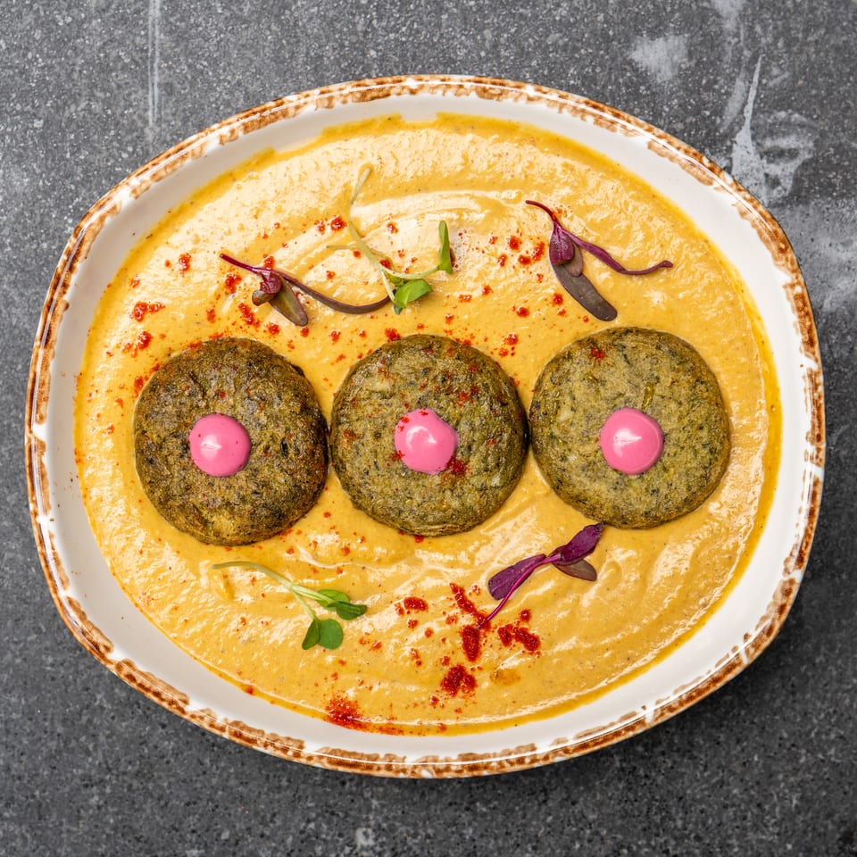 Three crispy herb patties topped with pink sauce, served in creamy golden sauce with microgreens and red spice.