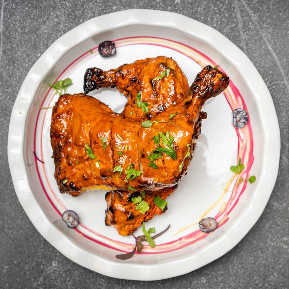Glazed grilled chicken pieces garnished with fresh herbs on a decorative plate, accompanied by green dipping sauce.